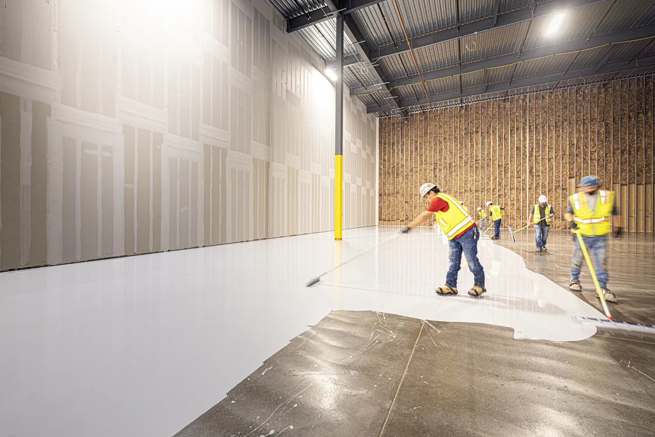 Workers spreading a grey floor coating with application tools